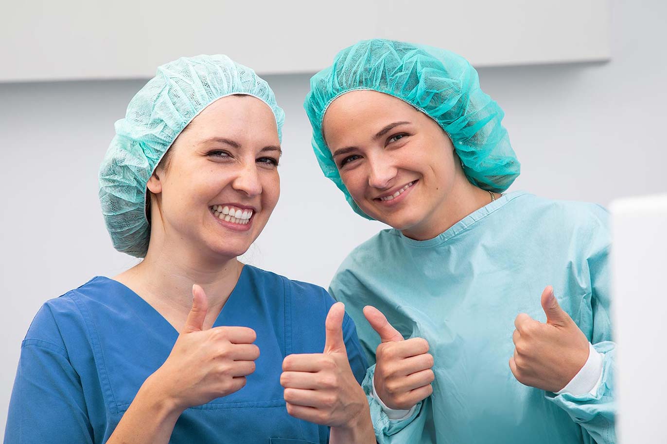 Zwei Frauen in medizinischer Kleidung zeigen Daumen hoch.