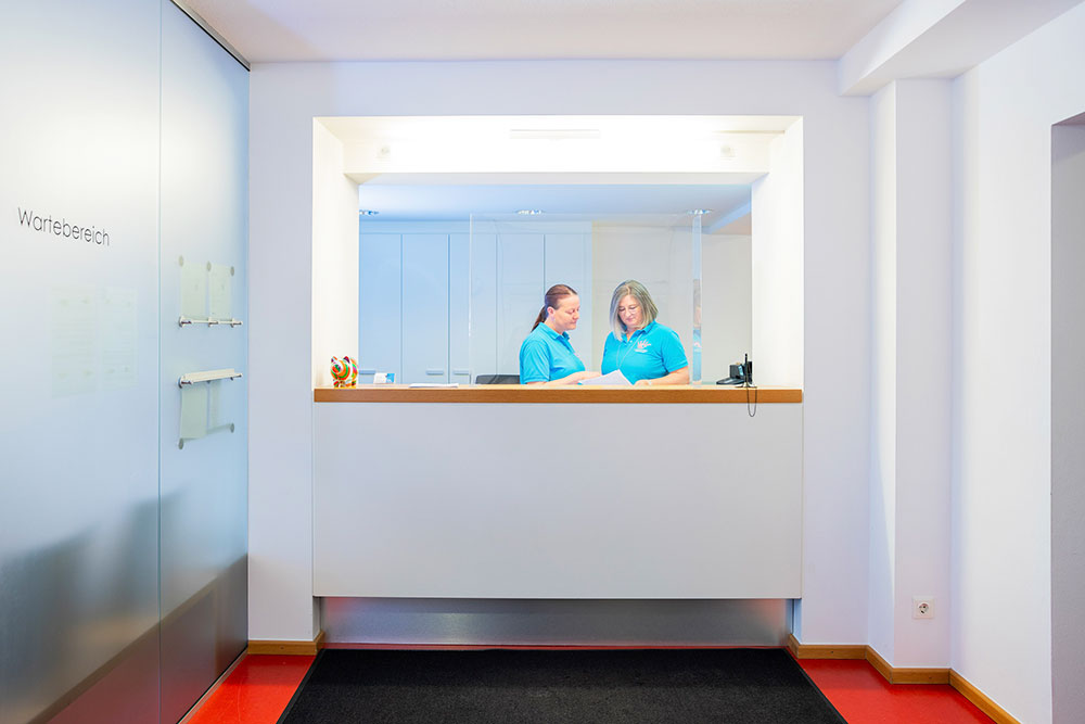 Empfangsbereich MVZ Grafenau Empfangsbereich mit zwei Mitarbeiterinnen, die Informationen austauschen.